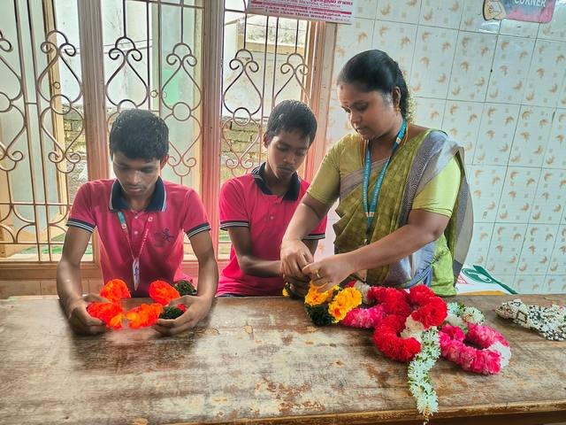 Children making flower garlands with their teacher